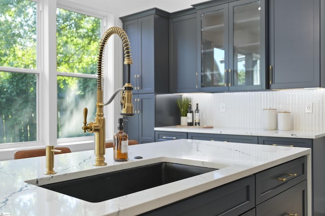 kitchen featuring decorative backsplash, glass insert cabinets, a sink, and light stone counters