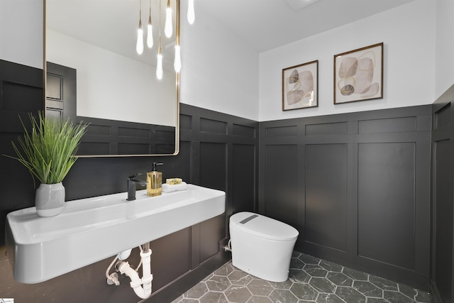 bathroom featuring a wainscoted wall, a decorative wall, and toilet