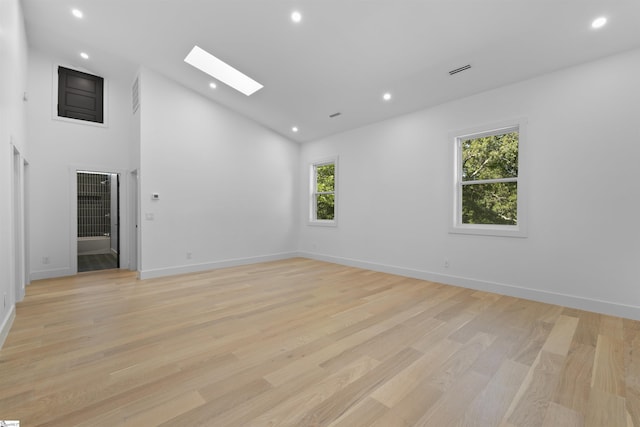 unfurnished room with light wood-type flooring, high vaulted ceiling, a skylight, and recessed lighting