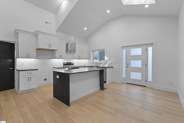 kitchen with high vaulted ceiling, stainless steel electric range, a center island, light wood-type flooring, and wall chimney range hood