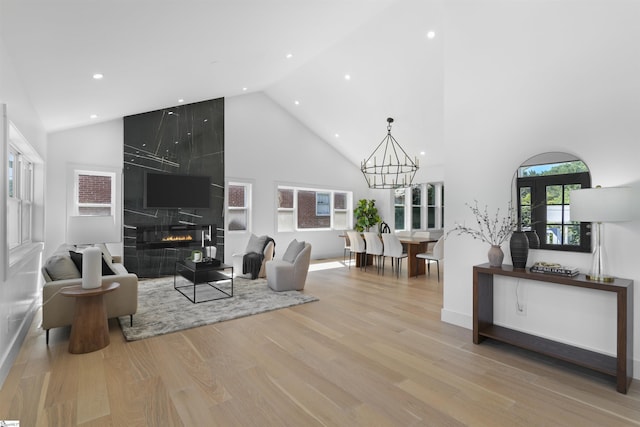 living room with high vaulted ceiling, a tile fireplace, light wood finished floors, recessed lighting, and an inviting chandelier