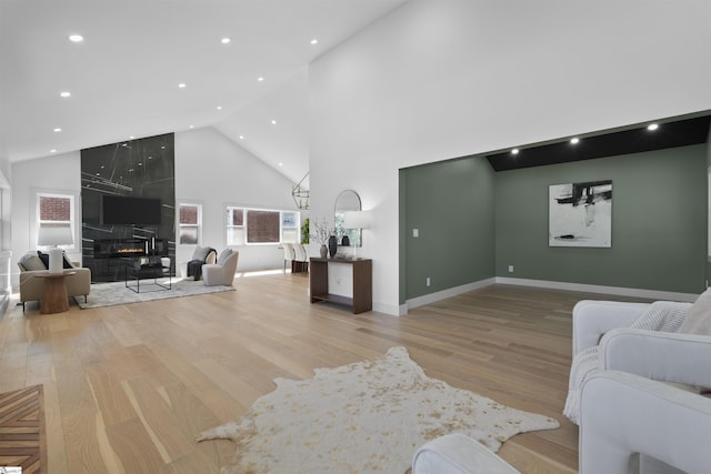 living area with high vaulted ceiling, a tiled fireplace, wood finished floors, baseboards, and recessed lighting
