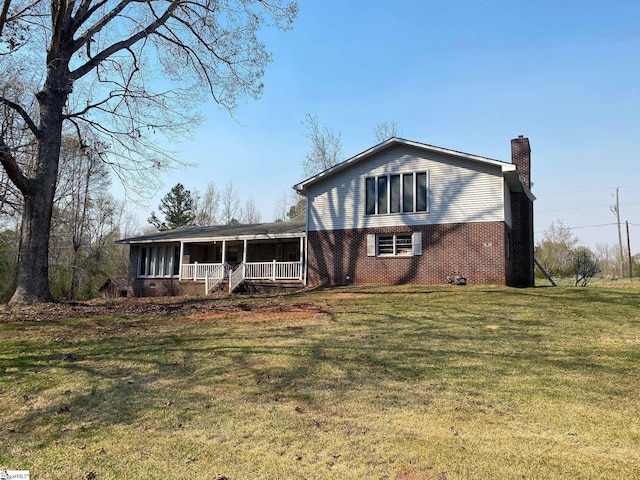 view of front of house featuring a chimney, a front yard, a porch, and brick siding
