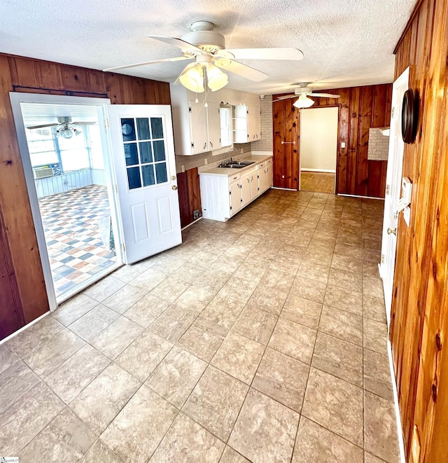 kitchen featuring a textured ceiling, wood walls, light countertops, ceiling fan, and white cabinetry