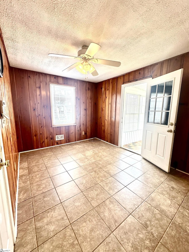 tiled spare room featuring a textured ceiling, wooden walls, and a ceiling fan