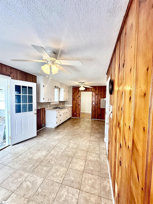 kitchen featuring light countertops, wood walls, a sink, and a ceiling fan