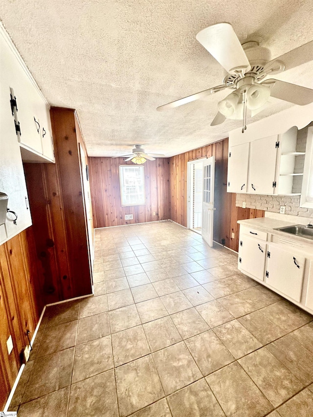 interior space featuring light countertops, a sink, a ceiling fan, white cabinetry, and wood walls