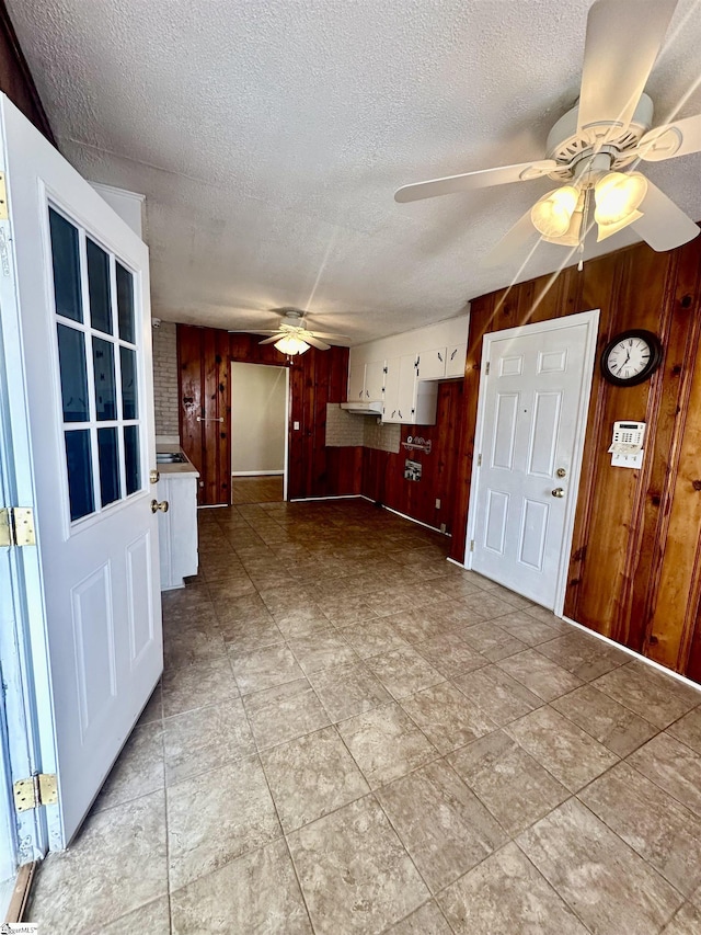 foyer with wood walls, a textured ceiling, and ceiling fan