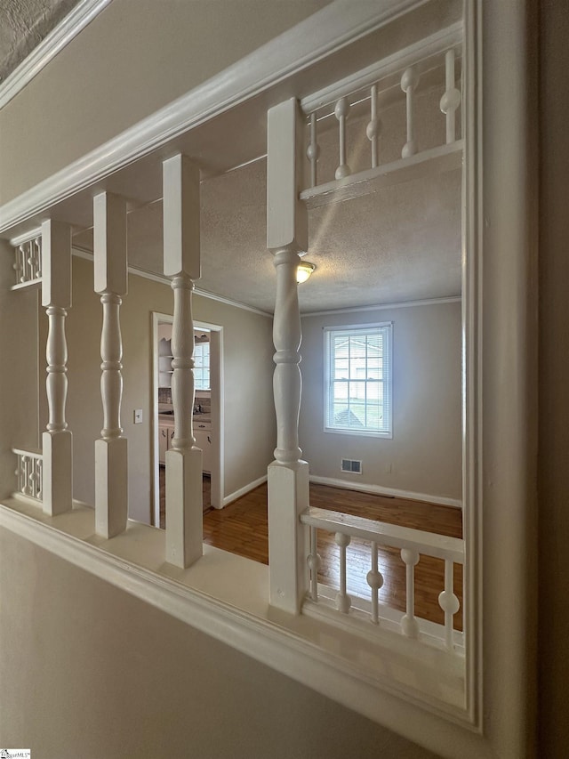 interior space featuring a textured ceiling, visible vents, crown molding, and wood finished floors