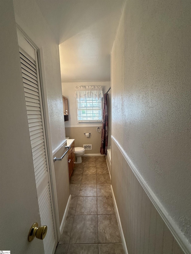 full bathroom featuring a wainscoted wall, toilet, tile patterned floors, vanity, and shower / bath combination with curtain