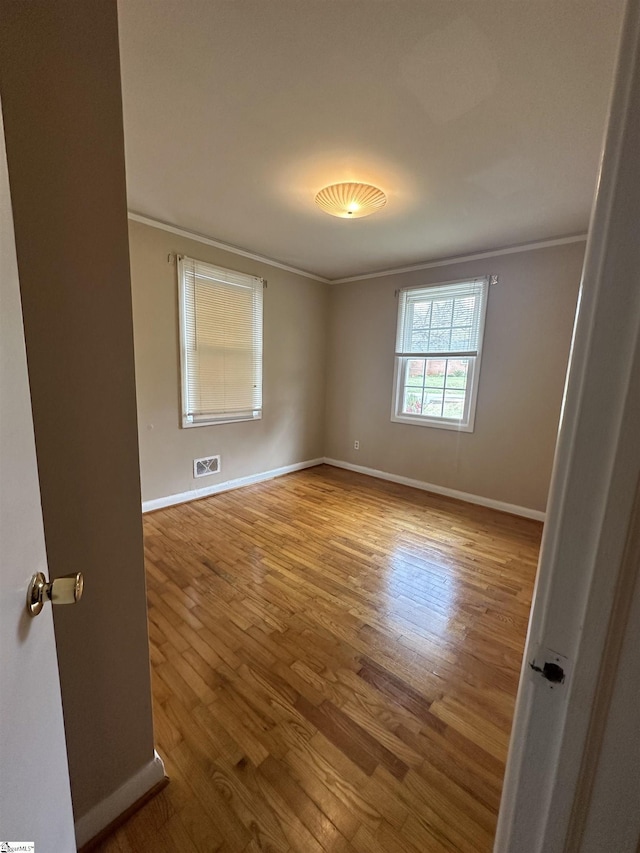 unfurnished room featuring wood finished floors, crown molding, baseboards, and visible vents