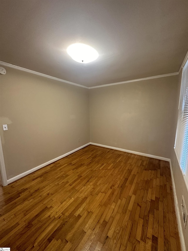 spare room with baseboards, wood finished floors, and crown molding