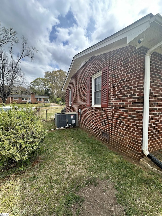 view of home's exterior featuring central air condition unit, a lawn, fence, and brick siding