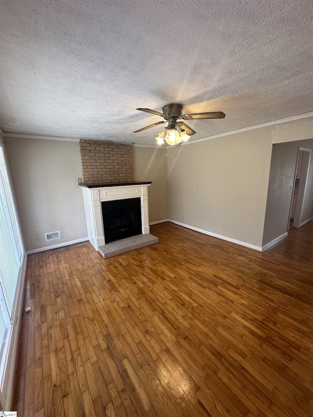 unfurnished living room with visible vents, a brick fireplace, ceiling fan, ornamental molding, and wood-type flooring