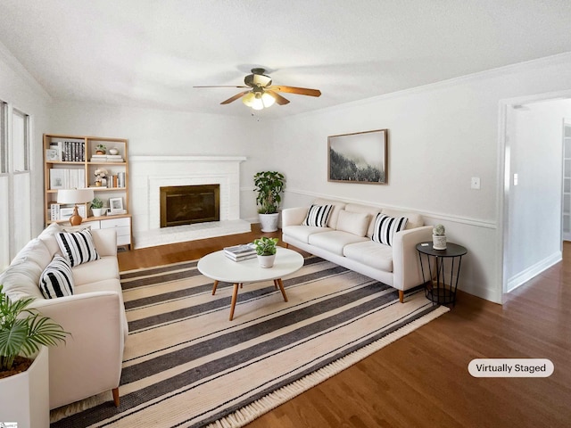 living area featuring a brick fireplace, ornamental molding, ceiling fan, and wood finished floors