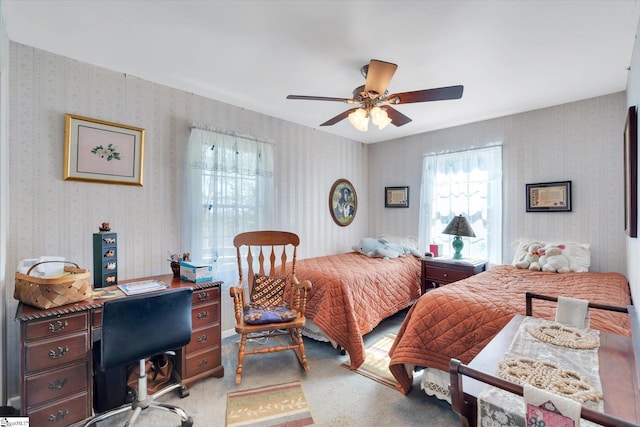 carpeted bedroom with wallpapered walls, multiple windows, and ceiling fan
