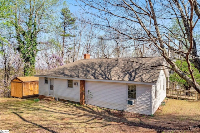 back of house with an outdoor structure, roof with shingles, entry steps, a yard, and a chimney