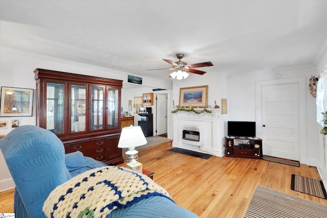 living room with heating unit, light wood-style flooring, a ceiling fan, and ornamental molding