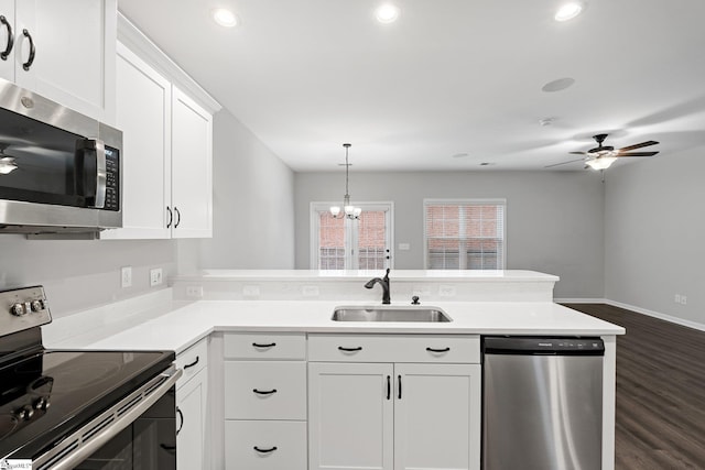 kitchen with light countertops, a sink, appliances with stainless steel finishes, a peninsula, and ceiling fan with notable chandelier