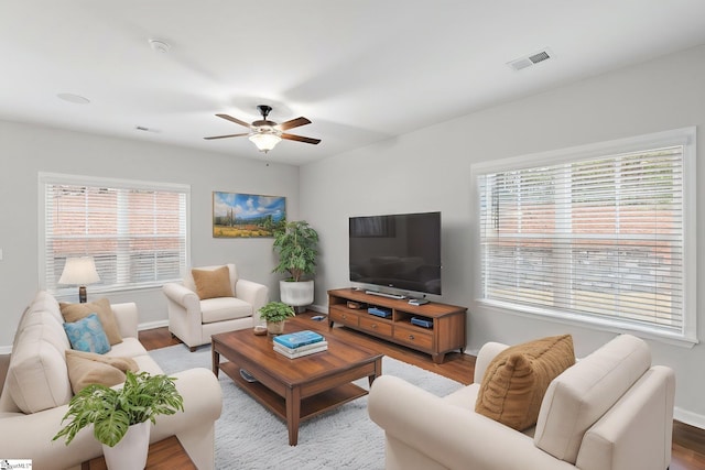 living room with baseboards, visible vents, wood finished floors, and a ceiling fan
