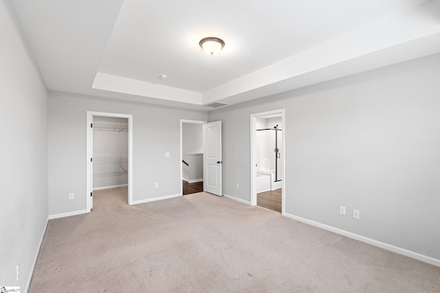 unfurnished bedroom with a tray ceiling, a spacious closet, carpet, baseboards, and visible vents