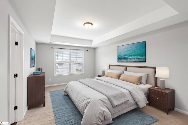 bedroom featuring light carpet, baseboards, and a raised ceiling