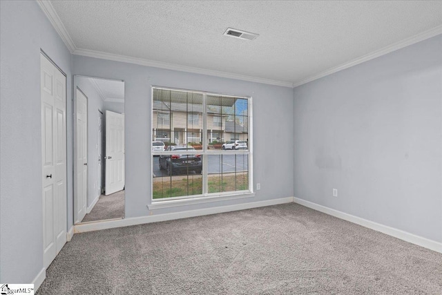 empty room with ornamental molding, carpet, a textured ceiling, and visible vents