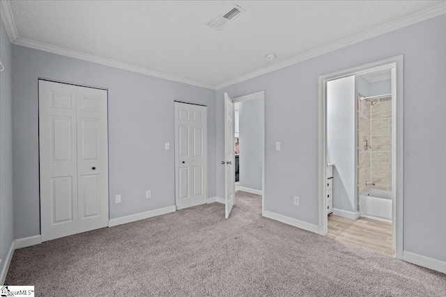 unfurnished bedroom featuring two closets, carpet flooring, crown molding, and visible vents