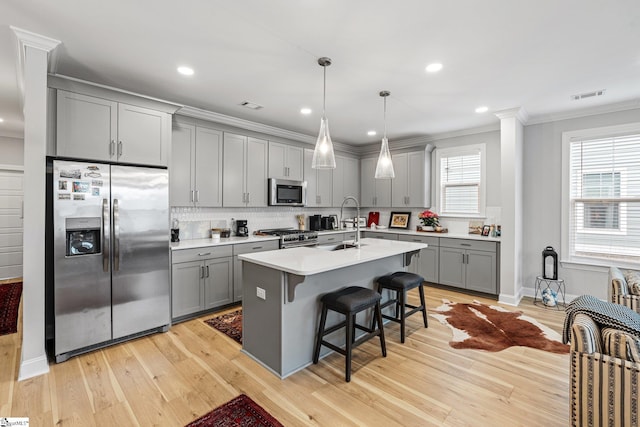 kitchen with a breakfast bar area, crown molding, light wood-type flooring, gray cabinets, and stainless steel appliances
