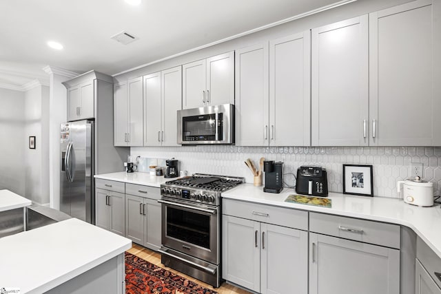kitchen with crown molding, gray cabinets, stainless steel appliances, decorative backsplash, and visible vents