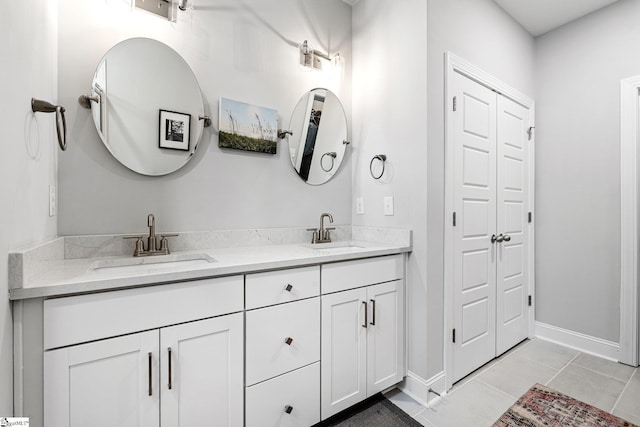 bathroom featuring baseboards, double vanity, a sink, and tile patterned flooring