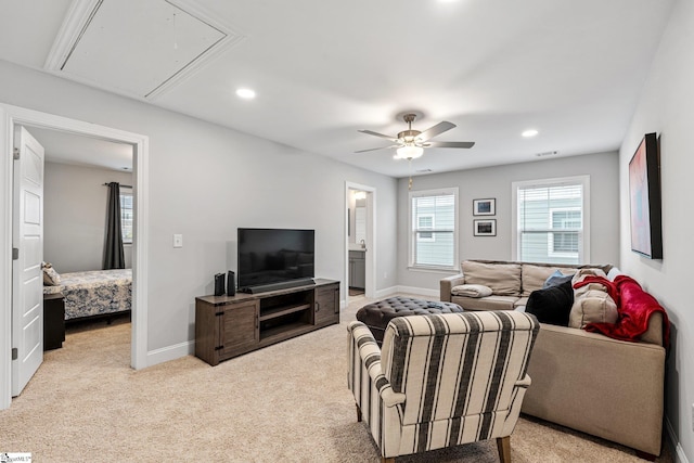 living area with attic access, light colored carpet, baseboards, and a ceiling fan
