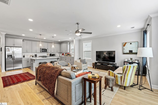 living area featuring visible vents, light wood-style flooring, ornamental molding, and a ceiling fan