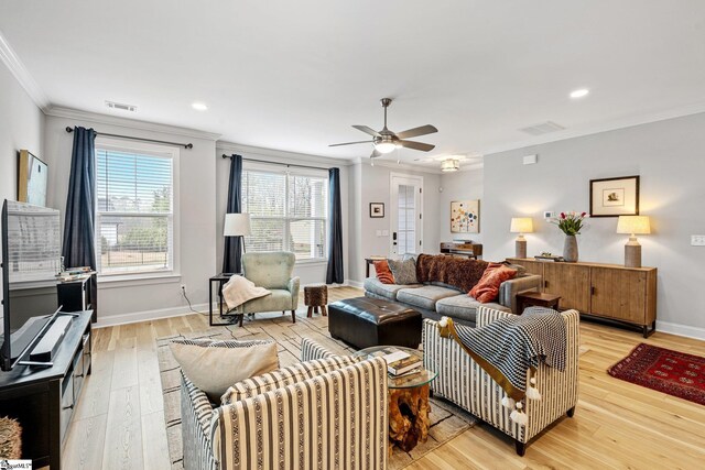 living room with light wood-type flooring, visible vents, ceiling fan, and ornamental molding