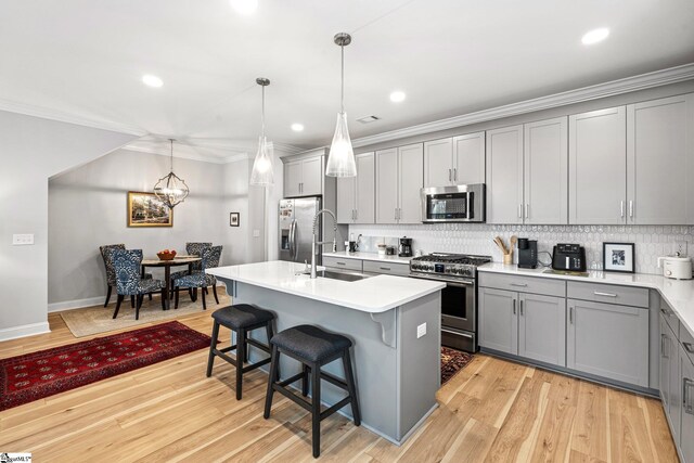 kitchen with crown molding, stainless steel appliances, tasteful backsplash, a sink, and gray cabinetry