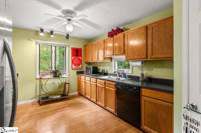 kitchen with a sink, dishwasher, dark countertops, light wood-style floors, and ceiling fan