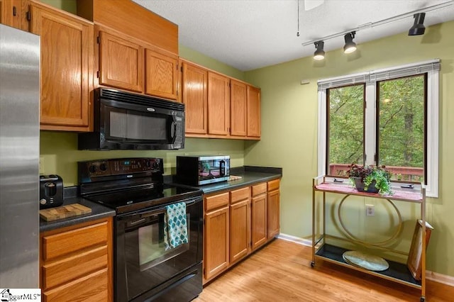 kitchen with light wood finished floors, brown cabinetry, baseboards, dark countertops, and black appliances
