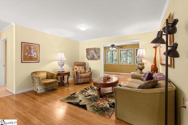living area featuring baseboards, ceiling fan, wood finished floors, and crown molding