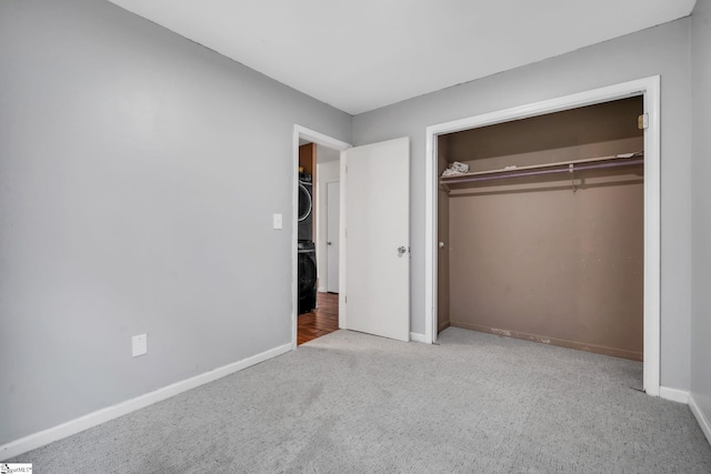 unfurnished bedroom with carpet flooring, a closet, baseboards, and stacked washer / drying machine