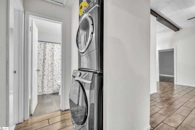 clothes washing area with stacked washer and dryer, wood tiled floor, laundry area, and baseboards