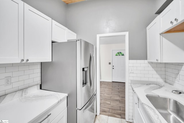 kitchen featuring white cabinetry, tasteful backsplash, stainless steel refrigerator with ice dispenser, a sink, and light stone counters