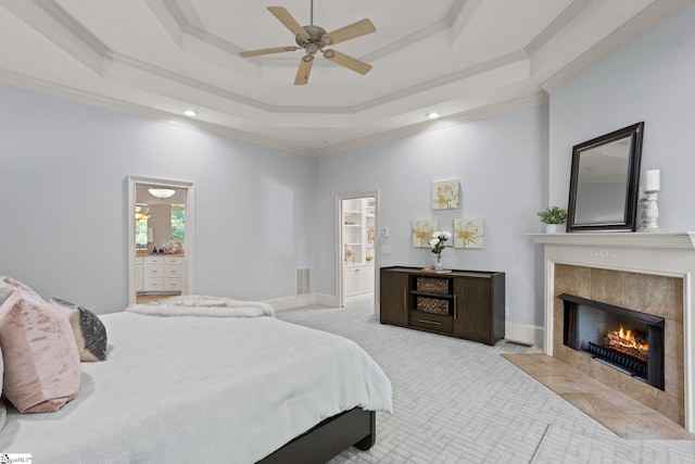 carpeted bedroom featuring a high end fireplace, crown molding, ensuite bathroom, and a raised ceiling