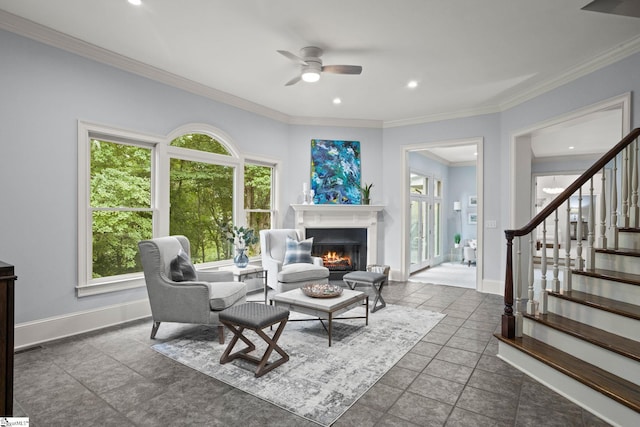 living area featuring stairs, crown molding, a ceiling fan, a warm lit fireplace, and baseboards