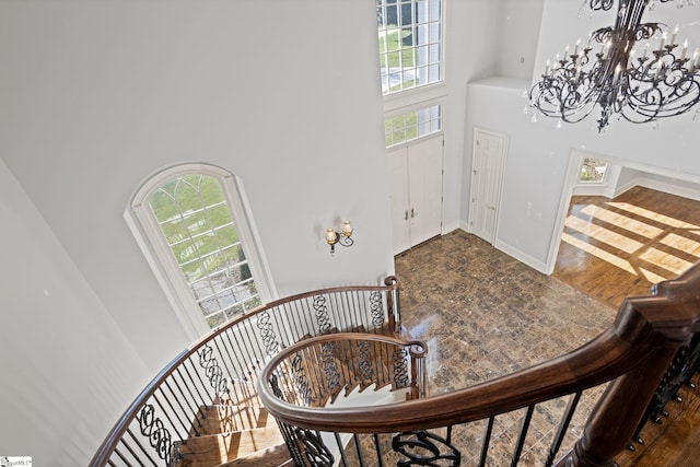 stairway with an inviting chandelier, a towering ceiling, and baseboards
