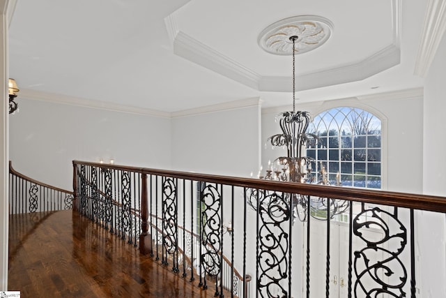 corridor with a tray ceiling, a notable chandelier, an upstairs landing, wood finished floors, and ornamental molding
