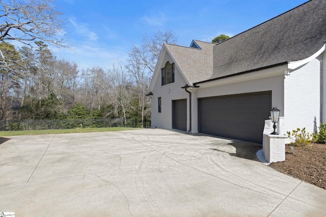 view of side of property featuring driveway, a shingled roof, fence, and brick siding