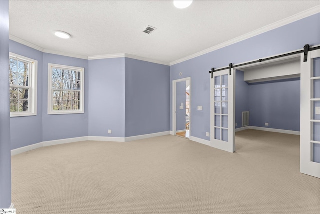 unfurnished bedroom featuring a barn door, a textured ceiling, visible vents, and crown molding