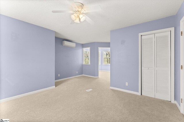 unfurnished bedroom featuring a closet, a textured ceiling, baseboards, light carpet, and a wall unit AC