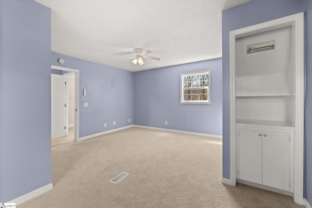 empty room featuring a ceiling fan, a textured ceiling, baseboards, light colored carpet, and visible vents