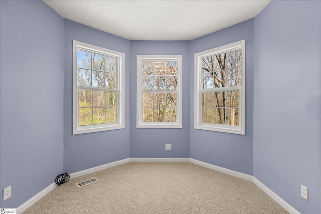 carpeted spare room featuring baseboards, visible vents, and a textured ceiling